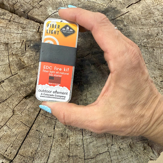 Hand holding a fiber light EDC fire kit on a wooden surface