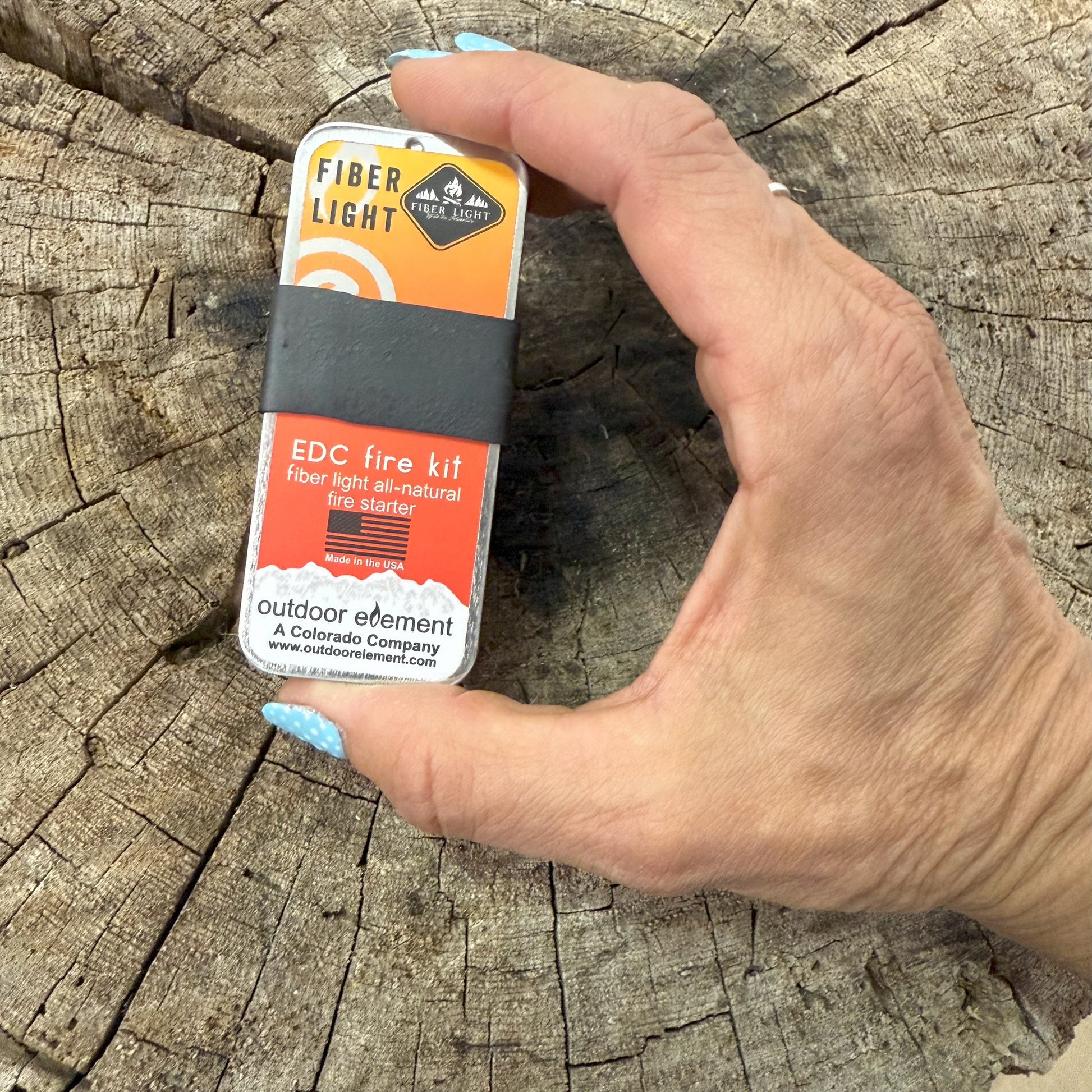 Hand holding a fiber light EDC fire kit on a wooden surface